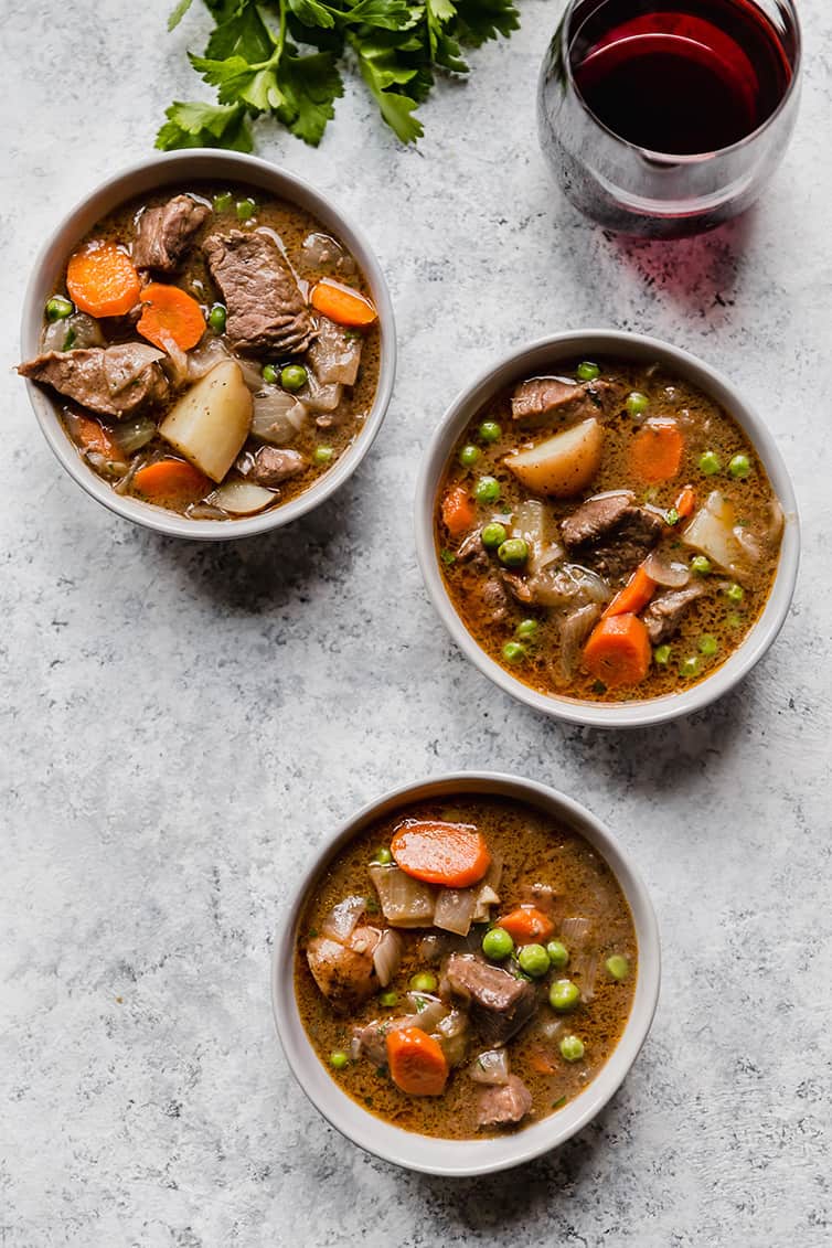 Three bowls of beef stew with a glass of red wine.