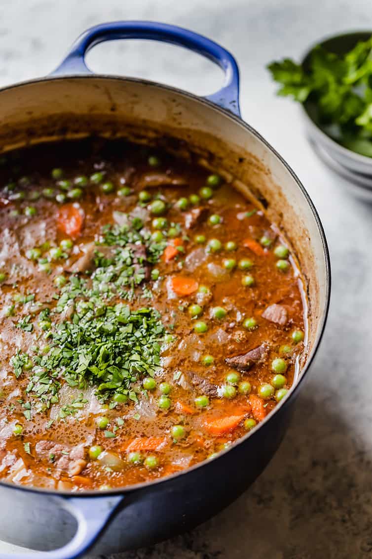 A pot of beef stew with peas and parsley added.