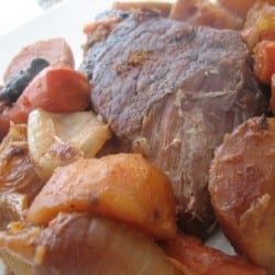 Pot roast with cooked potatoes, carrots, onions, and mushrooms on a plate.