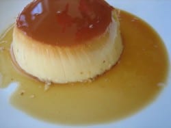 Flan on a white plate toped with caramel.