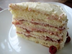 A slice of layer cake with raspberry preserves and cream cheese frosting sandwiched between 4 cake layers on a white plate.