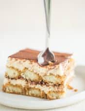 A piece of tiramisu on a plate with a fork going down into it.