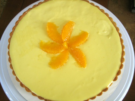 Overhead image of orange cream tart garnished with orange slices on a white plate before slicing.