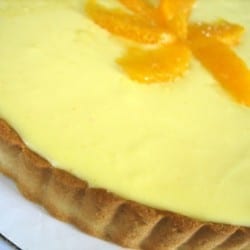 Orange cream tart before slicing on a white plate.