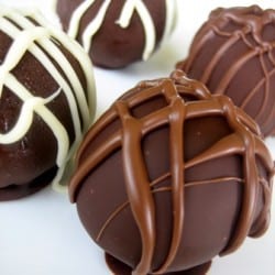 4 cheesecake truffles dunked in dark chocolate with a chocolate drizzle on top.
