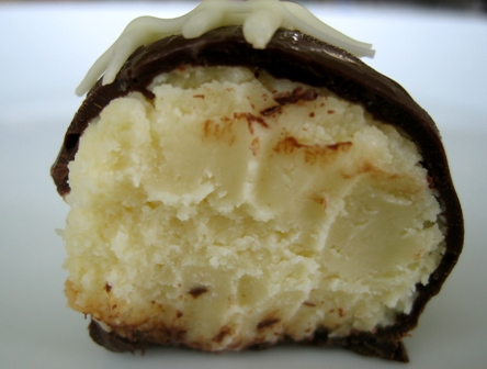 Cheesecake truffle with a chocolate coating cut in half showing the inside texture.