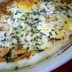 Baked eggs topped with herbs and cheese on a plate with a spoon.