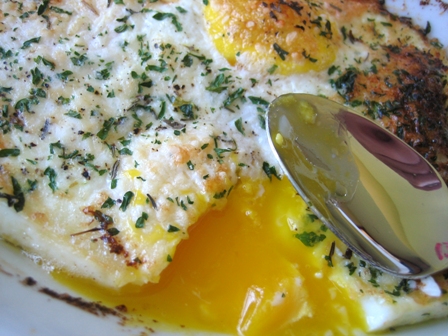 Baked eggs topped with herbs and cheese on a plate with a spoon.