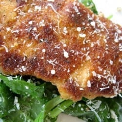 Cooked chicken breast coated in parmesan and breadcrumbs on top of a salad.