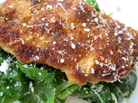 Cooked chicken breast coated in parmesan and breadcrumbs on top of a salad.