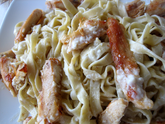 Fettuccini pasta noodles topped with alfredo sauce and pieces of chicken.