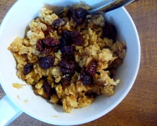 Baked oatmeal with raisins and dried berries in a white bowl with a spoon.