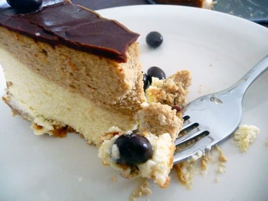 Slice of coffee and espresso layered cheesecake with a bite taken on a white plate with a fork.