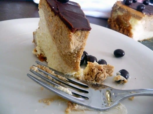 Slice of coffee and espresso layered cheesecake with a bite taken on a white plate with a fork.