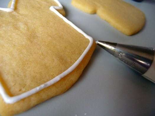 Using a piping tip to pipe a border of royal icing onto a sugar cookie.