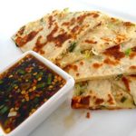 Scallion pancakes with a ginger dipping sauce on a white plate.