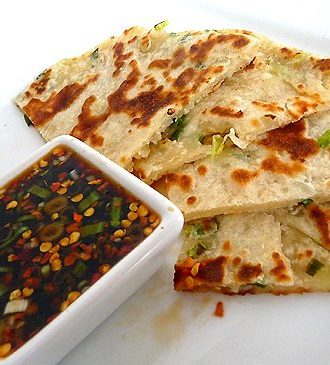 Scallion pancakes with a ginger dipping sauce on a white plate.