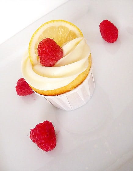 Lemon limoncello cupcake topped with frosting, a lemon slice, and raspberry.