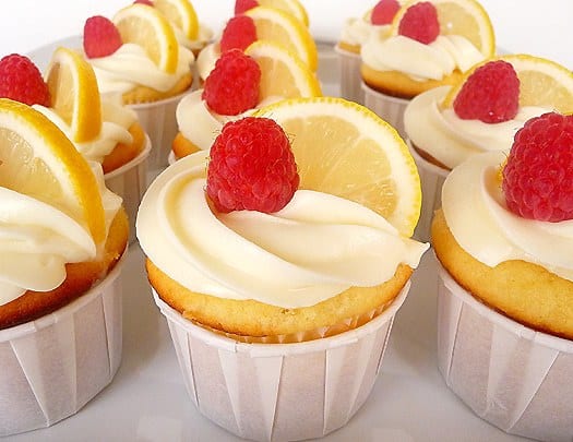 Lemon cupcakes topped with frosting, lemon slices, and fresh raspberries.