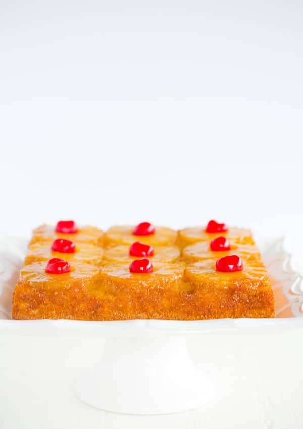 A pineapple upside down cake set on a square white cake dish.