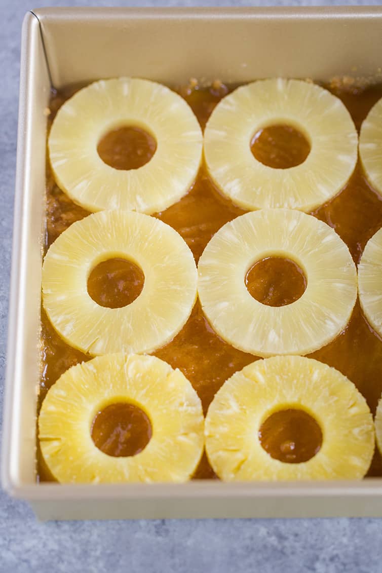 Slices of pineapple set atop a butter and brown sugar filling in a square pan.