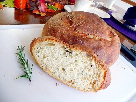 Slice of potato rosemary bread and the loaf of bread on a cutting board.