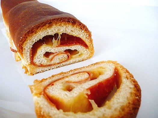 Loaf of soft cheese and pepperoni bread sliced in half showing the swirl inside on a white plate.