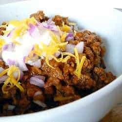 Chili in a bowl topped with sour cream, shredded cheese, and diced onion.