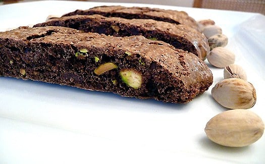 Pieces of chocolate pistachio biscotti on a white plate with pistachios.