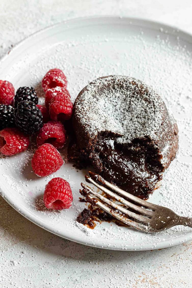 Chocolate lava cake on a white plate with a fork and raspberries.