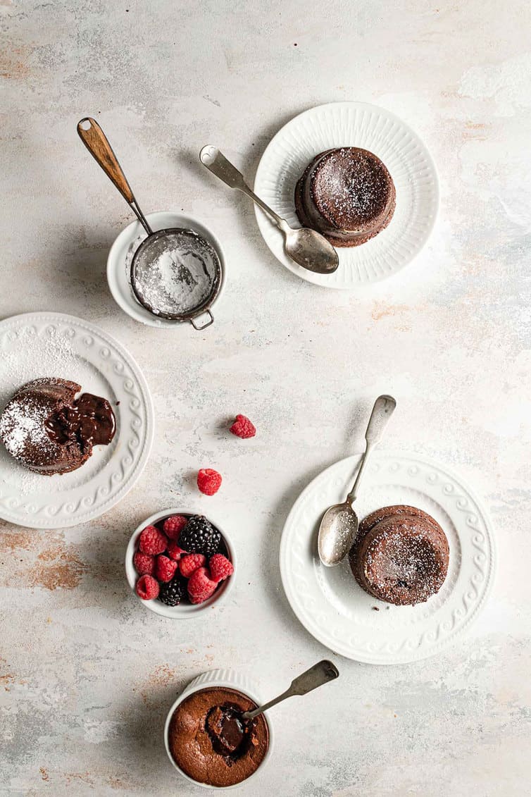 An overhead photo of chocolate lava cakes on white plates with a bowl of berries.