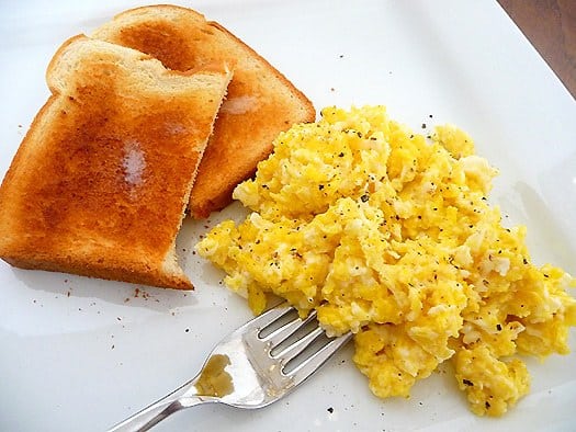 Scrambled eggs and toast on a white plate with a fork.