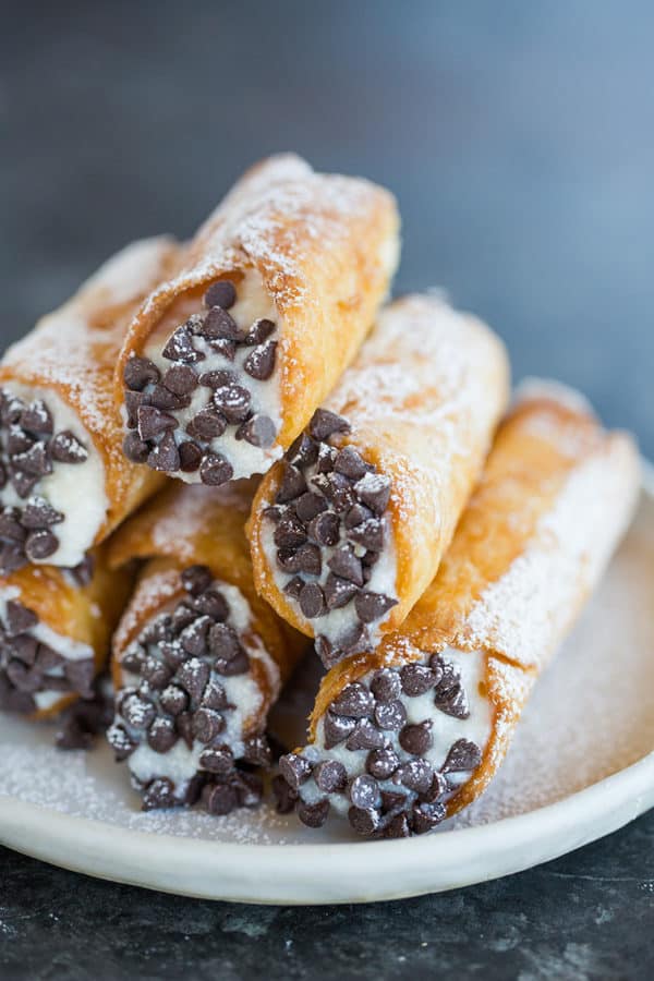 A stack of homemade cannoli on a plate with the ends dipped in chocolate chips.