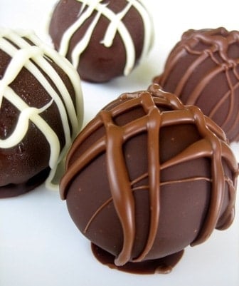 4 cheesecake truffles dunked in dark chocolate with a chocolate drizzle on top.
