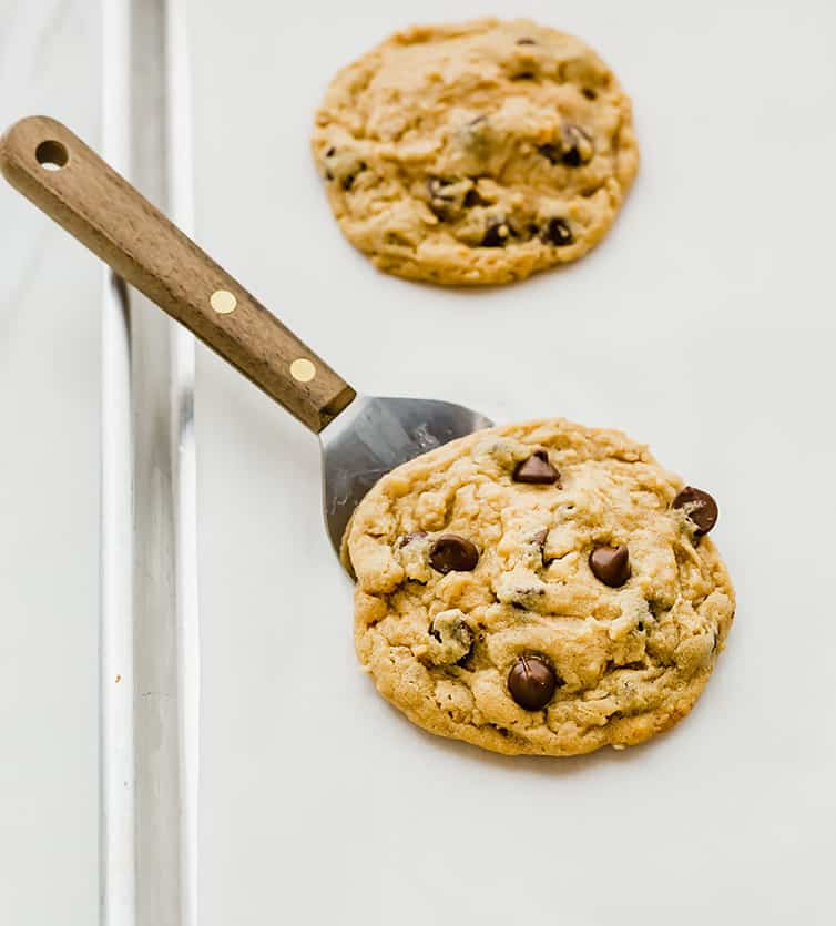 A spatula slid under a peanut butter-oatmeal chocolate chip cookie on a baking sheet.