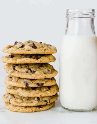 A stack of peanut butter-oatmeal chocolate chip cookies next to a glass bottle of milk.