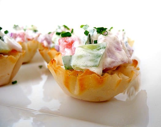 Cucumber tomato bruschetta appetizer pastry cups on a white plate.