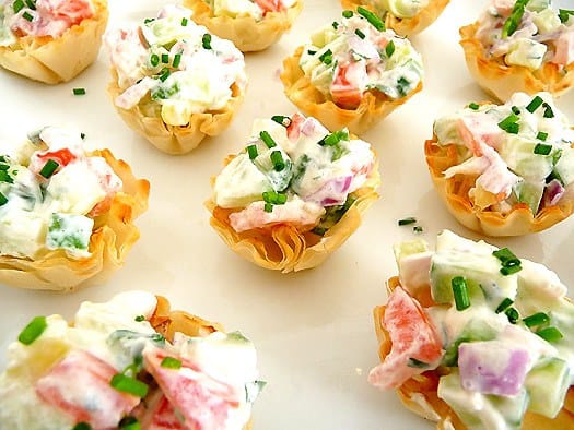Cucumber tomato bruschetta appetizer pastry cups on a white plate.