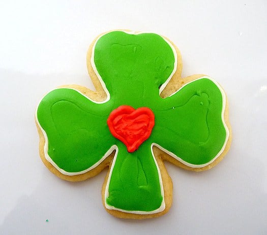 Shamrock sugar cookie with green icing and a red heart in the center.