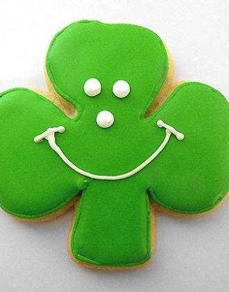 Shamrock sugar cookie with green icing and a white smiley face.