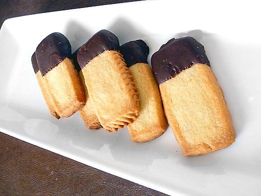Shortbread cookies with the ends of each cookie dipped in chocolate on a white serving tray.