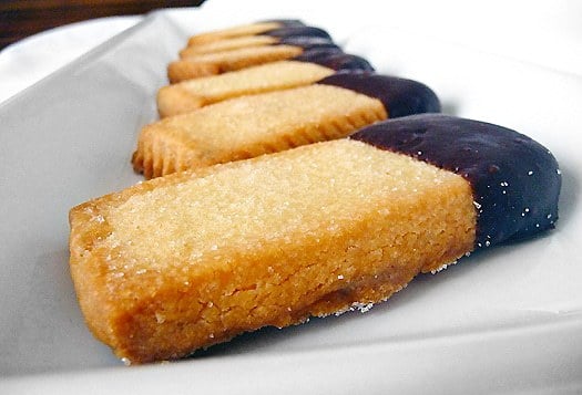 Shortbread cookies with the ends of each cookie dipped in chocolate on a white serving tray.