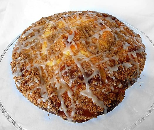 Overhead view of coffee cake with sweet cheese filling and vanilla icing on a glass cake stand.
