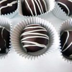 6 dark chocolate truffles in paper candy liners on a white plate.