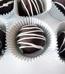 6 dark chocolate truffles in paper candy liners on a white plate.