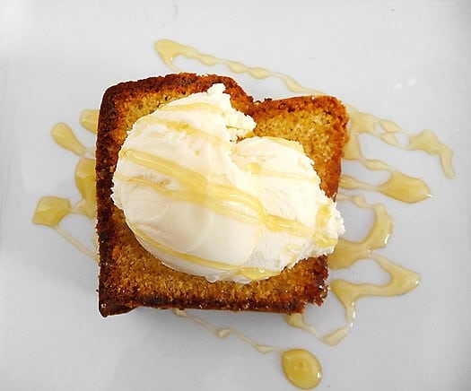 Slice of honey vanilla sour cream pound cake topped with a scoop of vanilla ice cream and a drizzle of honey on white plate.