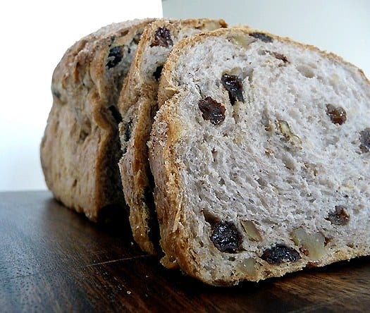 Slices of cinnamon raisin walnut bread on a wood serving board.