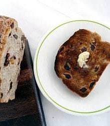 Slice of cinnamon raisin walnut bread on a white plate topped with a pat of butter.