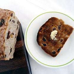Slice of cinnamon raisin walnut bread on a white plate topped with a pat of butter.