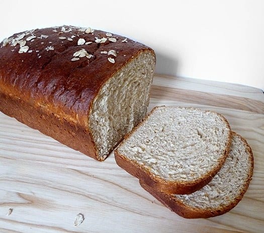 Loaf of honey oatmeal sandwich bread with 2 slices cut.